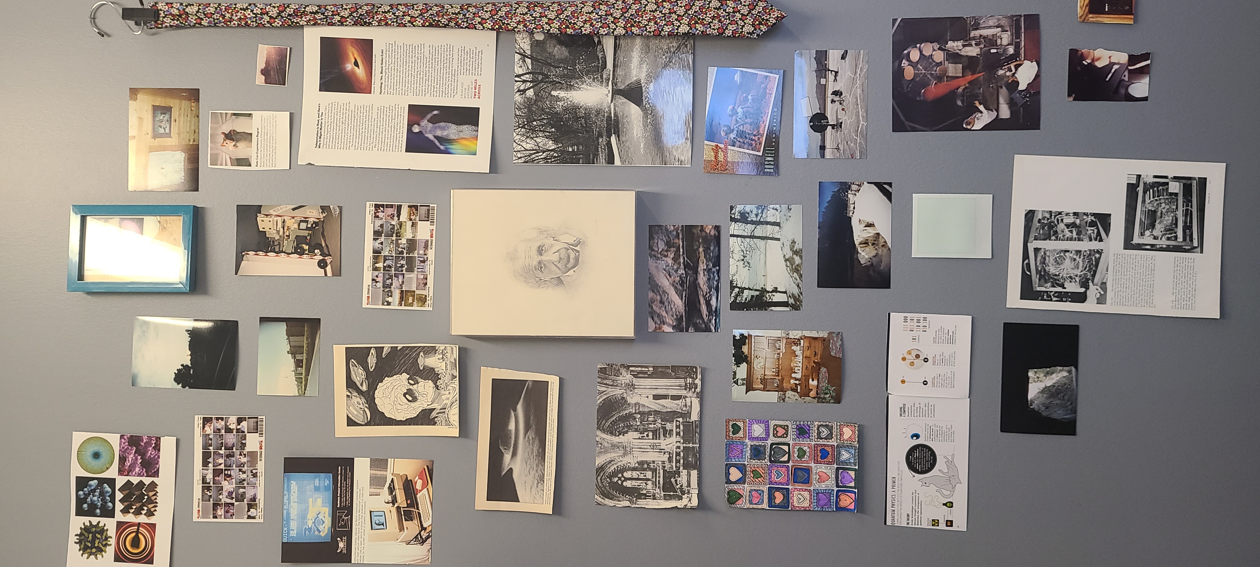 wall collage of weird old photos and a pencil drawing of albert einstein. there's some magazine pages and clippings and post cards and things. mostly alien and science themed.